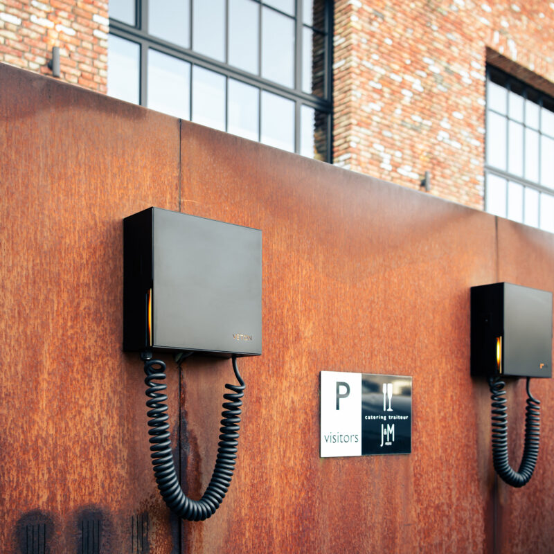 DSC 0375 Two Veton Wall Plus chargers on a corten steel facade at the entrance, visitor signage alongside.